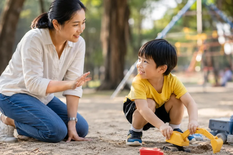 คุณแม่นั่งคุยกับลูกชายที่กำลังเล่นรถตักทรายในสวน